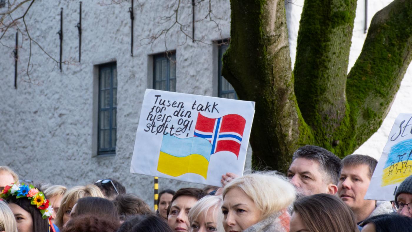 Bilde av tilskuere og en plakat med skriften "tusen takk for din hjelp og støtte".