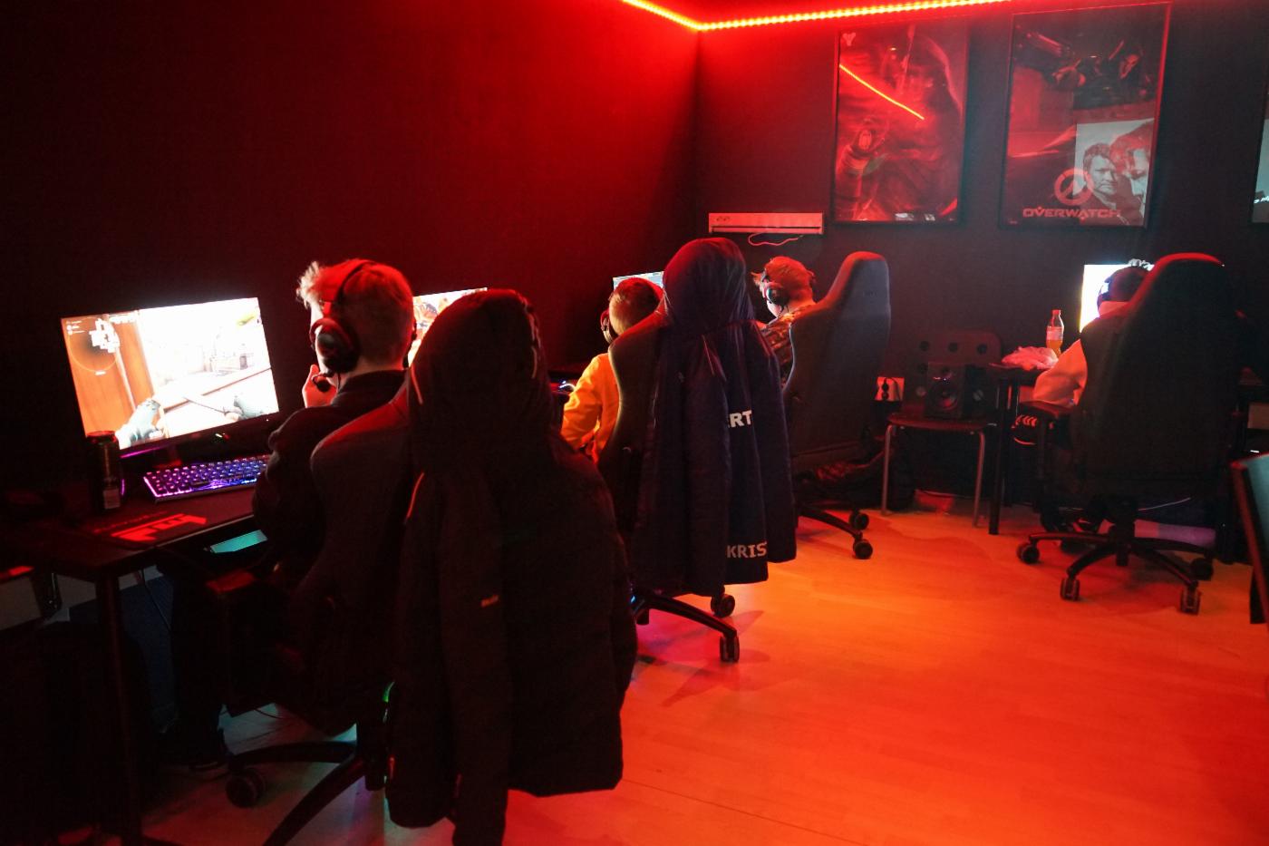 En gjeng ungdommer gamer på hver sin pc i et rød-oransje rom. 