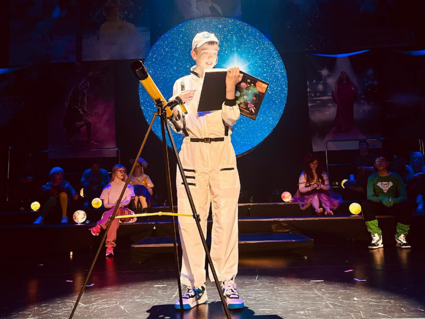 En gutt står på scenen med en stjernekikkert og en stjernehimmel bak seg.