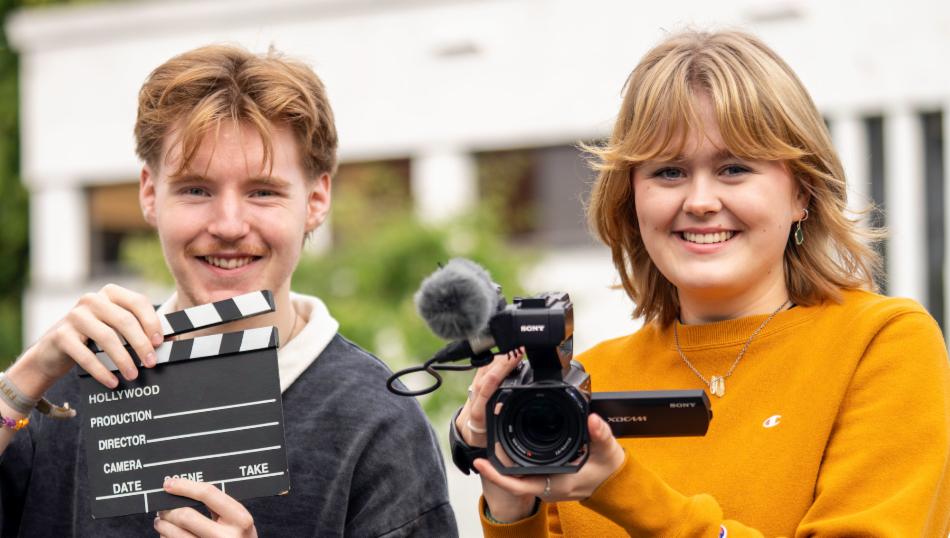 En jente og en gutt holder filmutstyr, mens de smiler til fotografen.