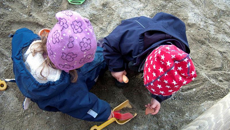 Bilde ovenfra av to barn som sitter tett sammen i sandkassen og ser på en spade