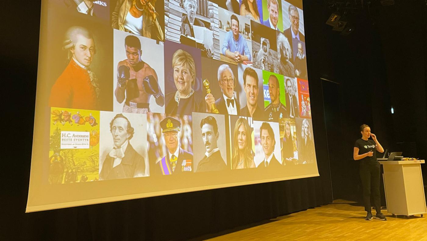 Storskjerm med bilder av kjente personer. Foredragsholder til høyre i bildet.