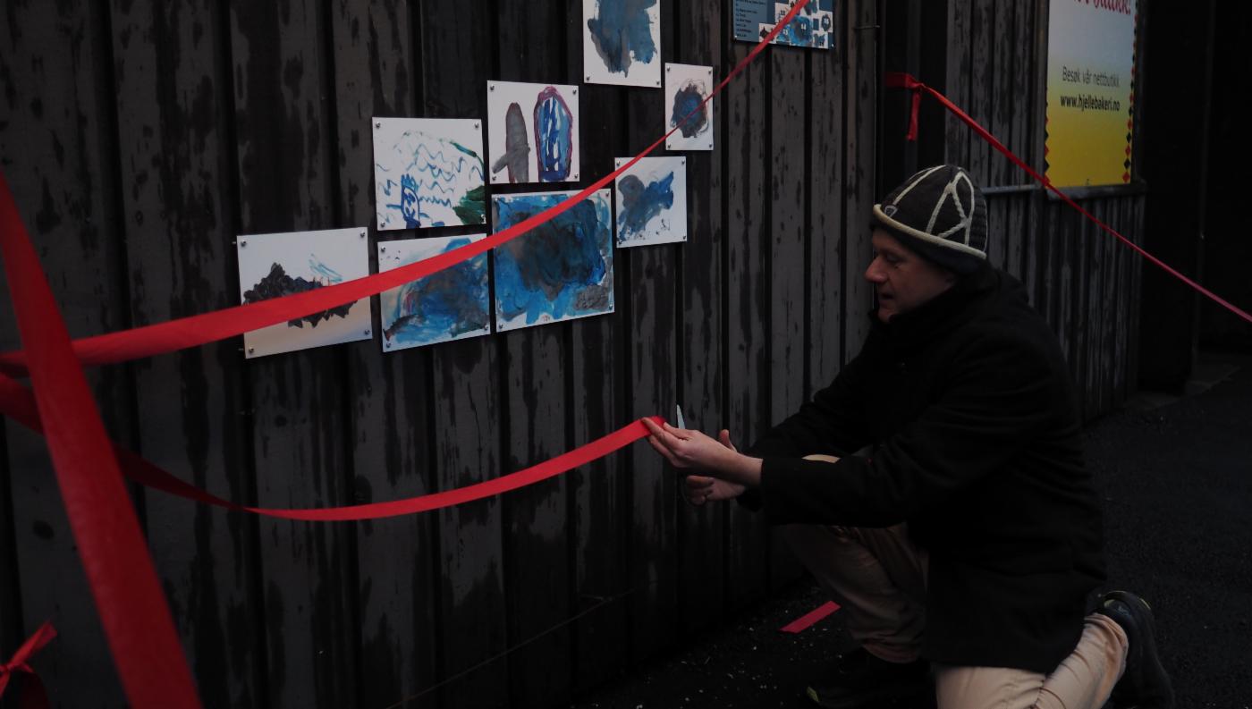 Mann klipper rød snor for å åpne kunstutstilling av barnetegninger