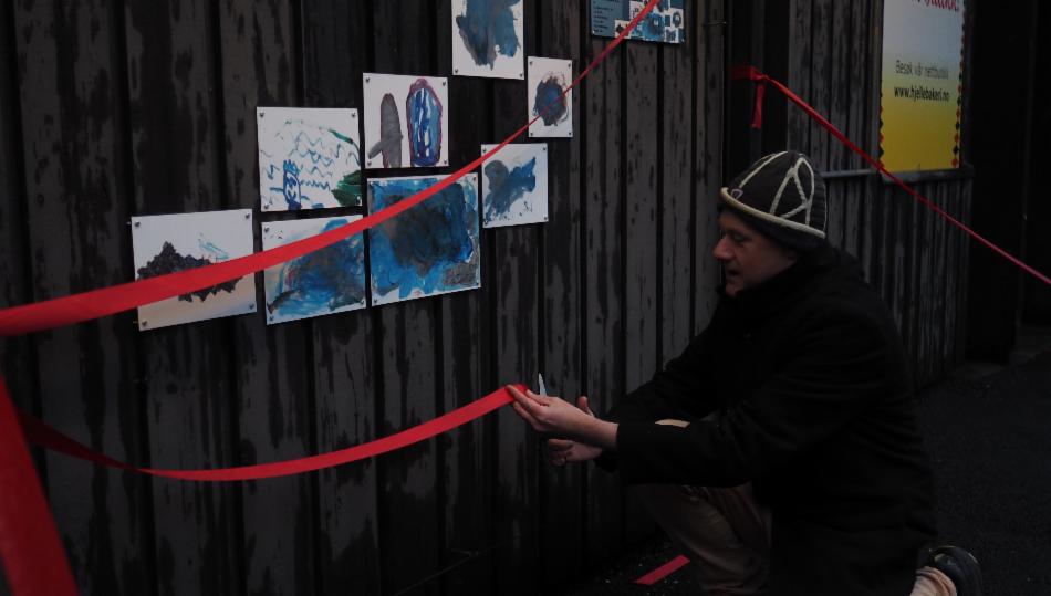 Mann klipper rød snor for å åpne kunstutstillingen av barnetegninger