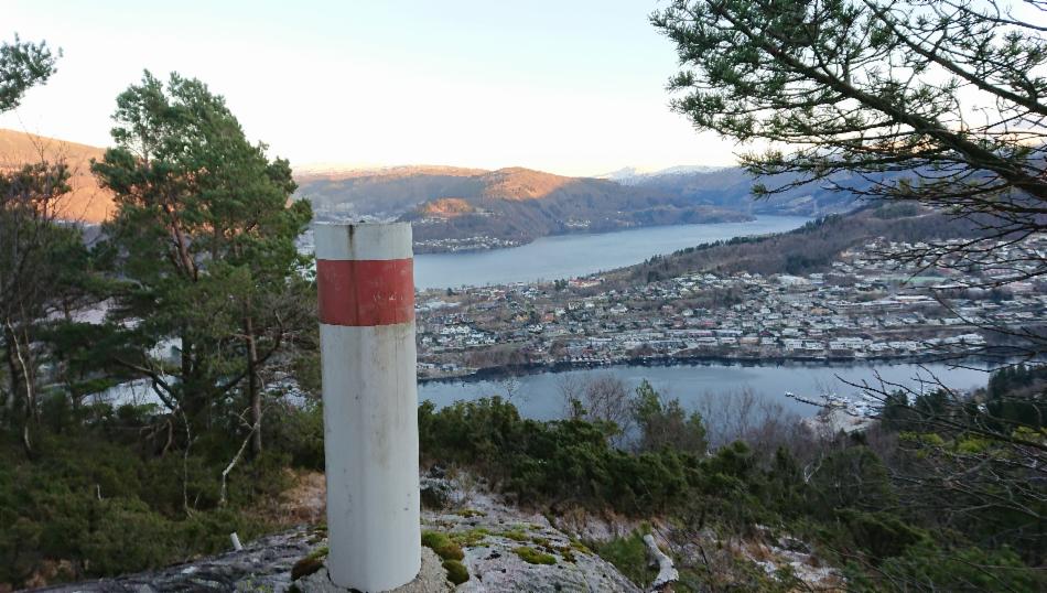 Hvit og rød søyle på fjellet med utsikt over fjorden