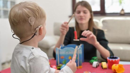 Barn med cochlea-implantat sitter ved bord og leker sammen med en voksen person.
