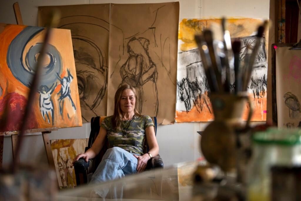 En dame sitter på en stol i et atelier mellom malerier