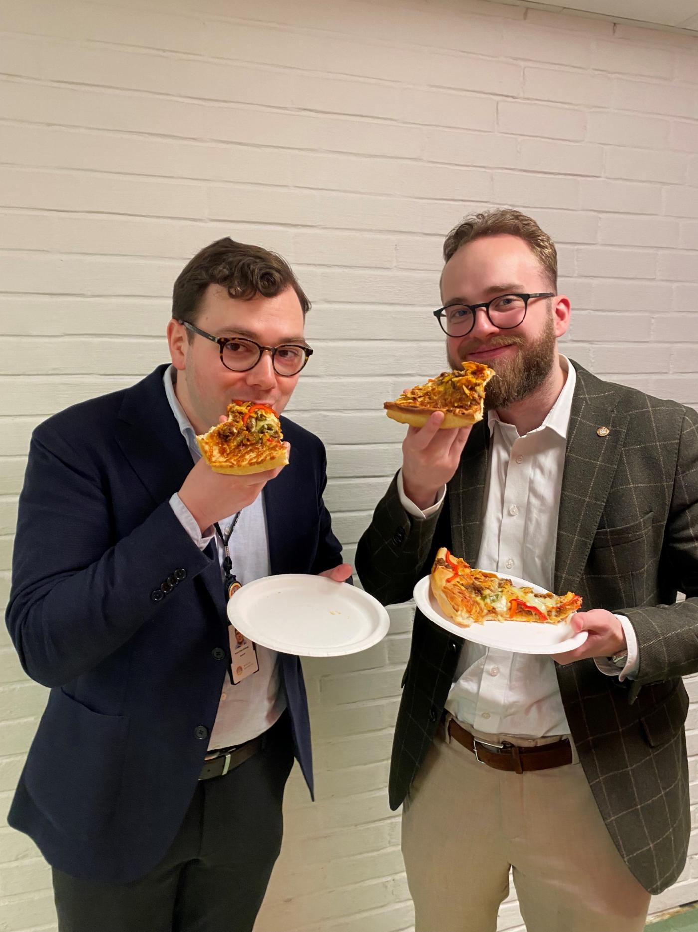 To unge menn i dressjakke spiser pizza. 
