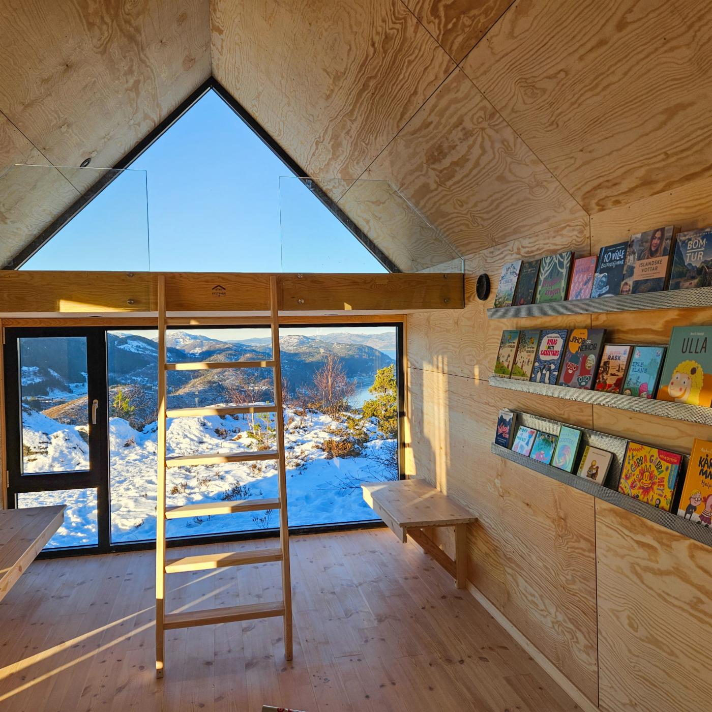Innsiden av hytten med turbibliotek og utsikt over Arnavågen. 
