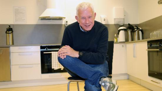 Finn Markussen viser yogaposisjon på kjøkkenstol.