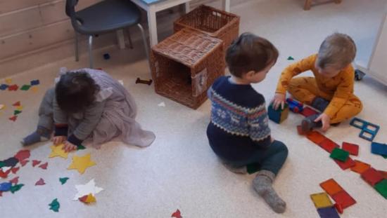 Tre barn sitter på gulvet og leker.