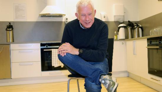 Finn Markussen viser yogaposisjon på kjøkkenstol.