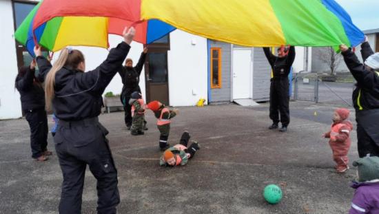 Ansatte med regnbuefarget fallskjerm over barn som leker