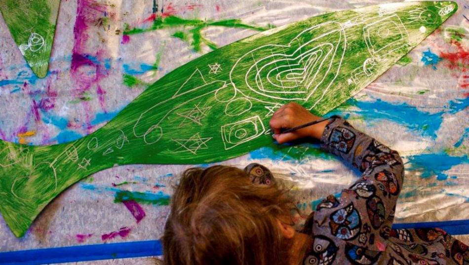 Et barn tegner figurer på en grønn fisk laget av papir.
