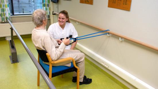 eldre dame trener armene med strikk sammen med kvinnelig helsearbeider