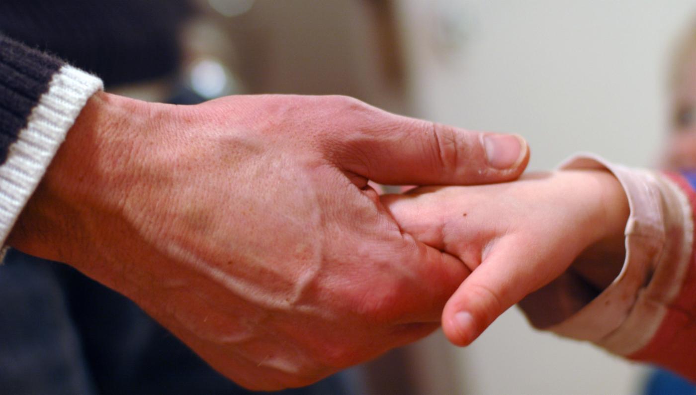 En voksen hånd holder varsomt en barnehånd.